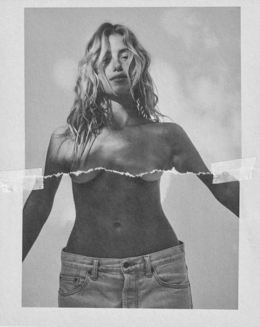 Monochrome studio portrait of a young adult female posing topless in jeans against a white background with harsh shadows.