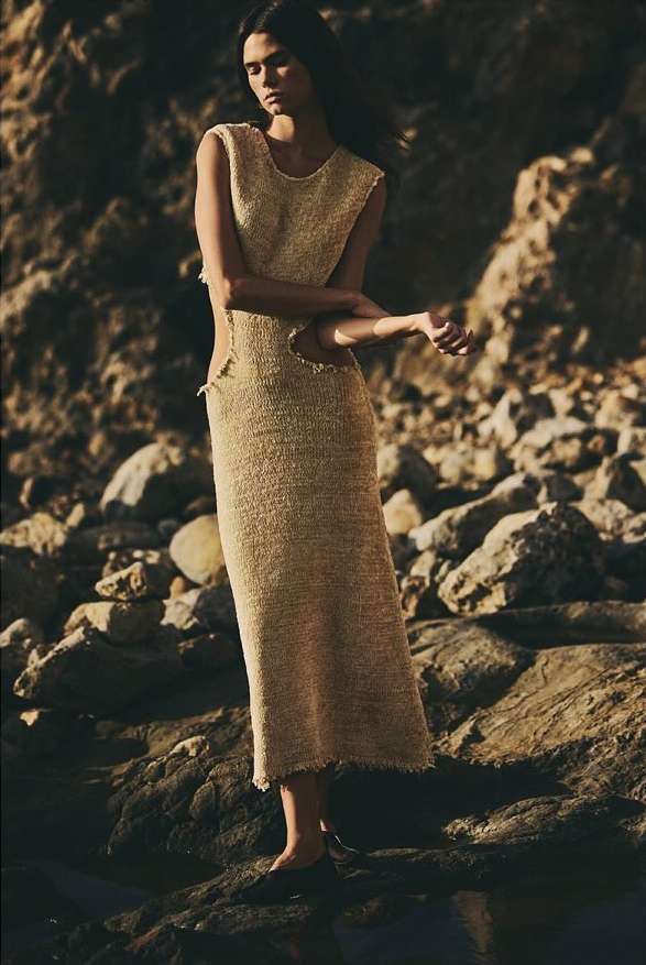 Model standing on rocky coastline wearing a textured sleeveless knit dress by Aaron Feaver.