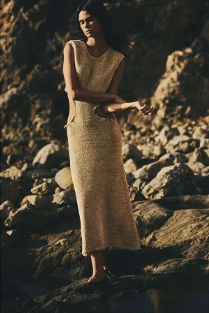 Model standing on rocky coastline wearing a textured sleeveless knit dress by Aaron Feaver.