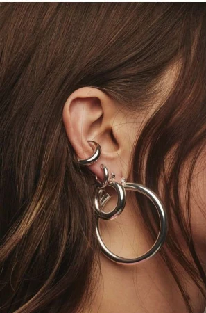 Close-up of an ear adorned with multiple polished silver hoop earrings and an ear cuff, framed by long brown hair.