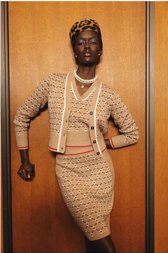 Model wearing a matching patterned knit cardigan and skirt with a leopard print hat standing against a wooden wall