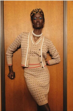 Model wearing a matching patterned knit cardigan and skirt with a leopard print hat standing against a wooden wall