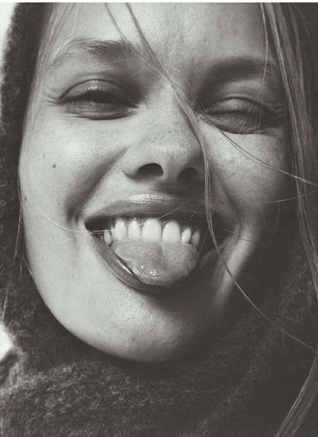 Close-up portrait of smiling woman with long blonde hair sticking out her tongue, shot by Aaron Feaver.