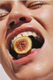 Close-up portrait of a person holding a sliced fig in their open mouth, captured by Aaron Feaver.