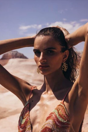 Woman in patterned top with hands behind her head standing outdoors in a desert landscape by Aaron Feaver