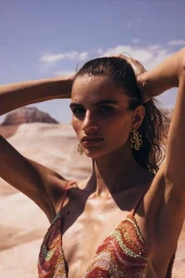 Woman in patterned top with hands behind her head standing outdoors in a desert landscape by Aaron Feaver