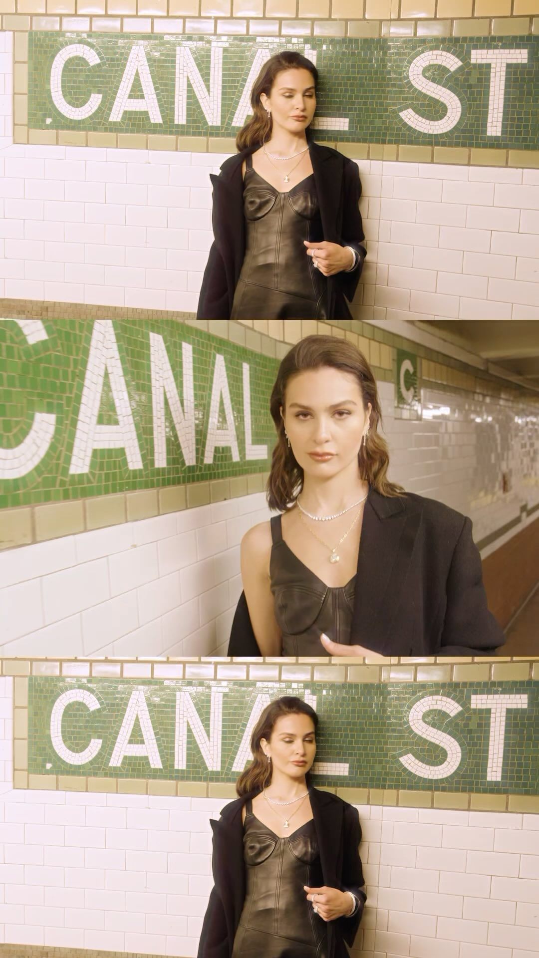 Woman in black dress and blazer poses against tiled 'Canal St' subway station wall, neutral expression, indoor setting, soft lighting.