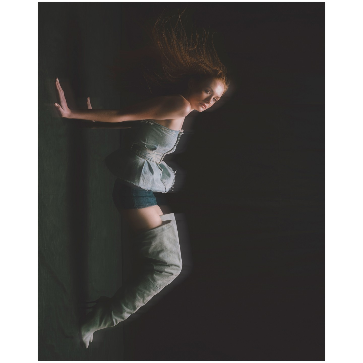 Woman in denim top and thigh-high boots posed against a dark backdrop by photographer Aart Verrips.