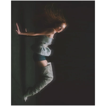 Woman in denim top and thigh-high boots posed against a dark backdrop by photographer Aart Verrips.