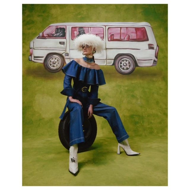 A woman in a denim jumpsuit and white boots sits on a tire in front of a vehicle illustration against a green backdrop, fashion shot.