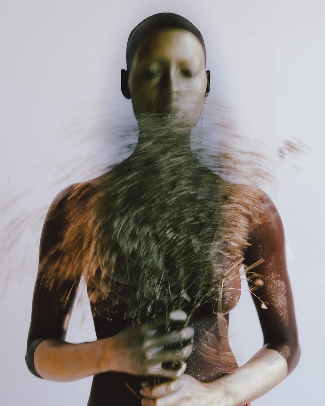 Artistic portrait of a bald adult with closed eyes and blurred grass details in the foreground against a plain white background.