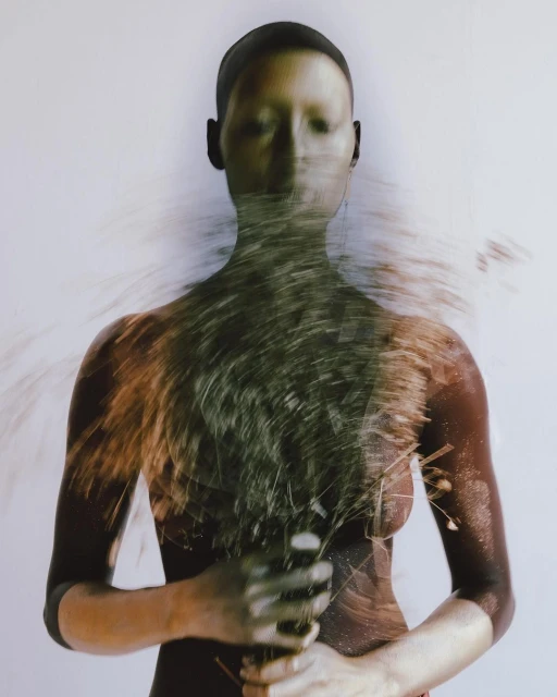 Artistic portrait of a bald adult with closed eyes and blurred grass details in the foreground against a plain white background.