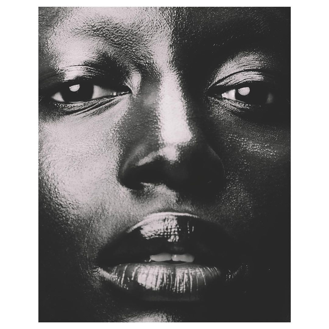 Close-up portrait of an adult female with dark skin and glossy lips, intense gaze, and dark background. Beauty and portrait photography.