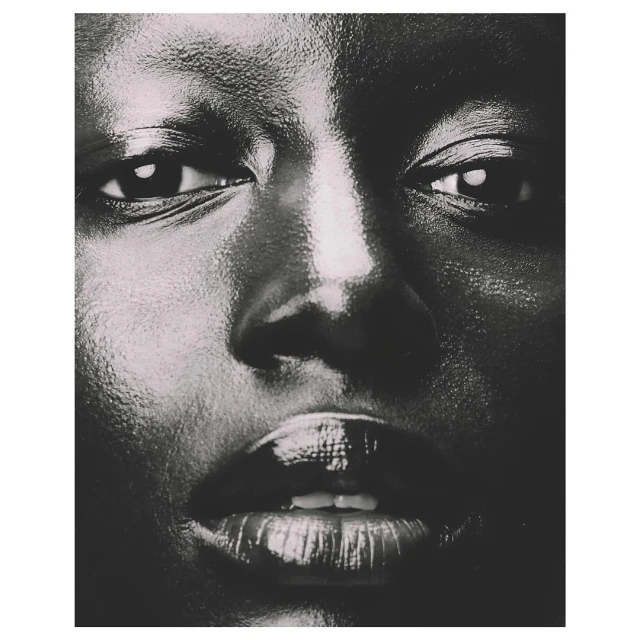 Close-up portrait of an adult female with dark skin and glossy lips, intense gaze, and dark background. Beauty and portrait photography.