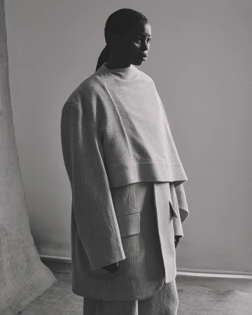 Monochrome portrait of a black woman in oversized beige suit, looking to the side in a studio setting with draped fabric.