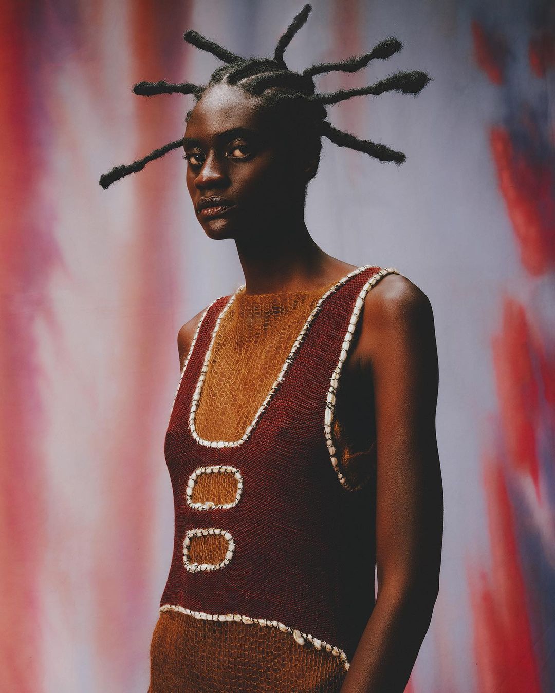Portrait of a Black female model wearing a knit top with unique hair against a mottled background in a studio with natural lighting.