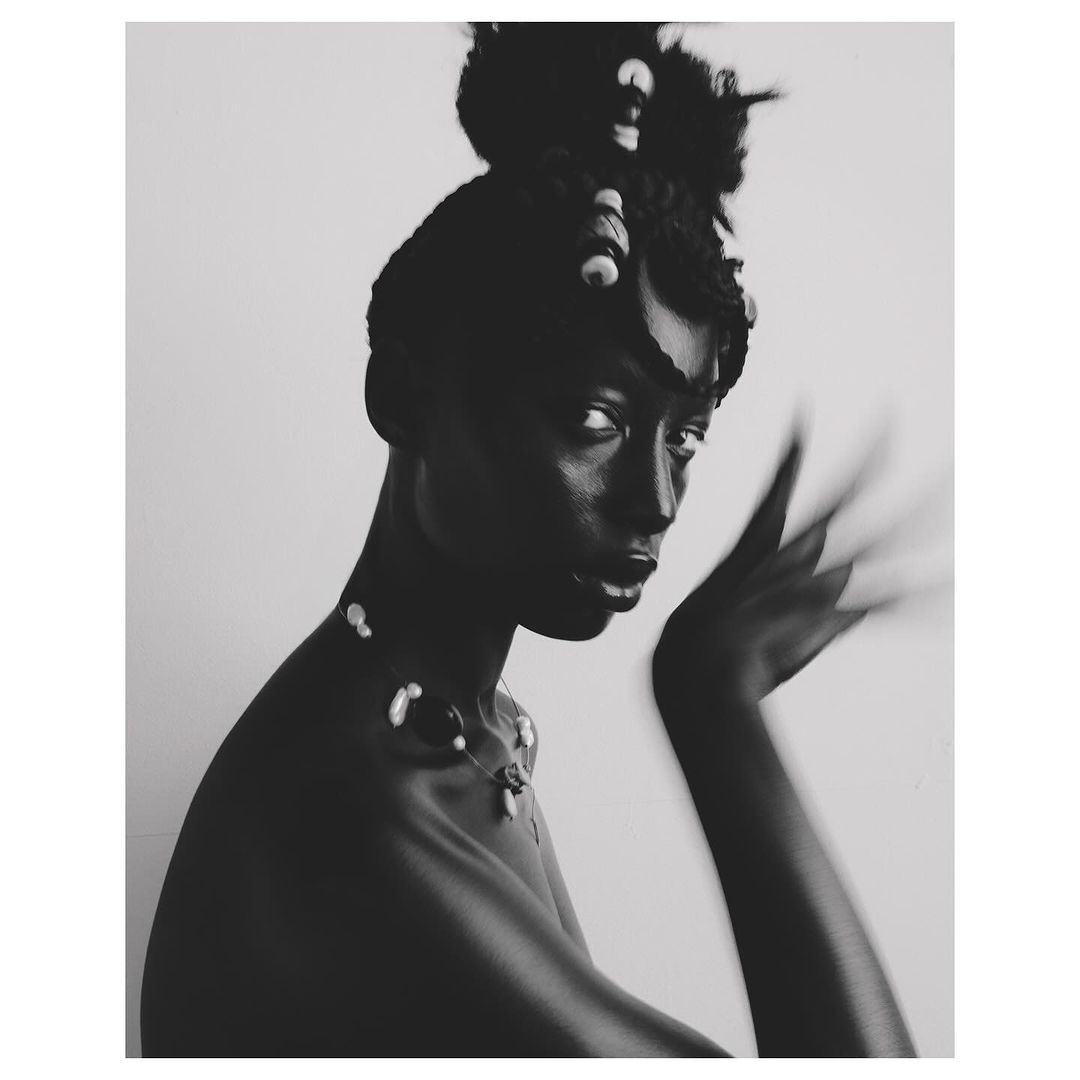 Black and white portrait of a woman wearing a beaded necklace with hair styled up and decorated with beads, by photographer Aart Verrips.