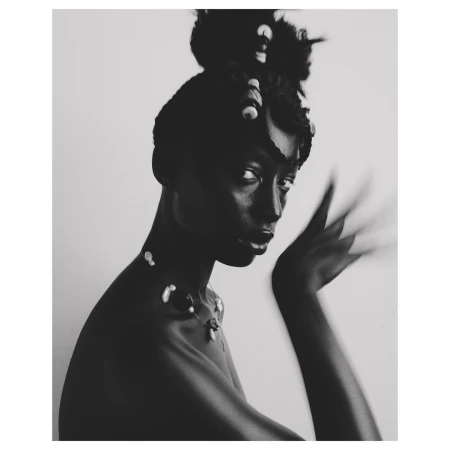 Black and white portrait of a woman wearing a beaded necklace with hair styled up and decorated with beads, by photographer Aart Verrips.