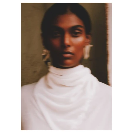 Portrait of a woman wearing a white high neck top and statement earrings captured with motion blur by photographer Aart Verrips.