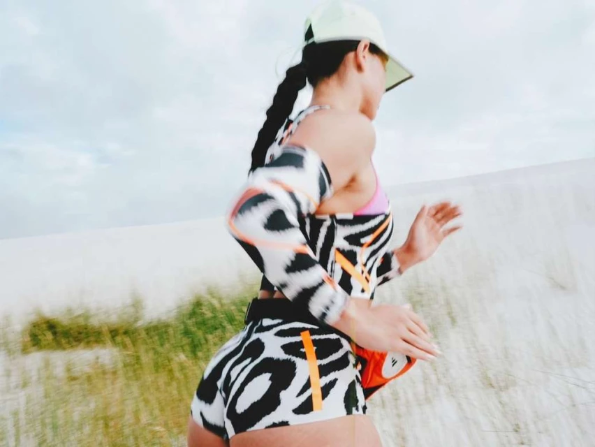 A person in athletic wear runs outdoors in a desert-like environment with a light-colored cap, zebra-striped top and shorts.
