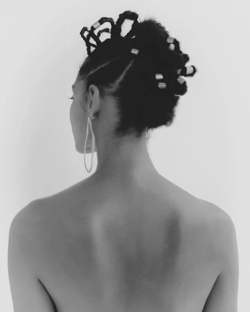 Woman's back and head showcasing intricate braided updo hairstyle adorned with silver beads, accented by teardrop earrings, against white.