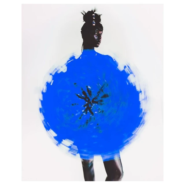 Artistic studio shot of a woman with dark skin wearing a blue circular garment against a neutral background. Long exposure effect.
