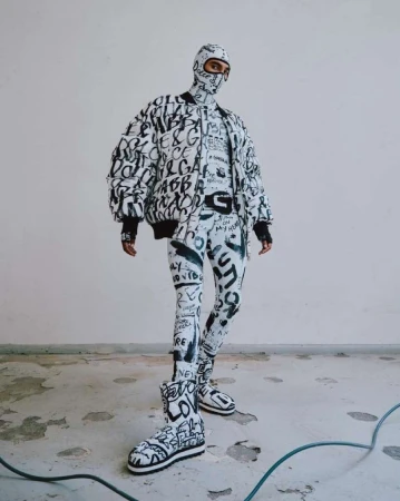 Person in full Dolce & Gabbana patterned outfit with jacket, balaclava, leggings, and boots, posing in a white indoor setting.