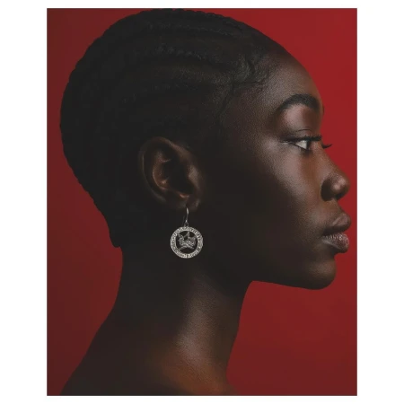 Profile portrait of a black woman wearing a round silver pendant earring against a solid red background