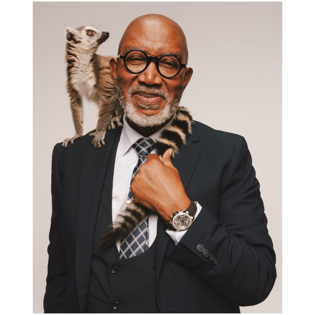 Elderly man in suit with lemur on shoulder, posing in studio. Business portrait of male with eyeglasses and exotic animal.
