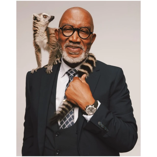 Elderly man in suit with lemur on shoulder, posing in studio. Business portrait of male with eyeglasses and exotic animal.