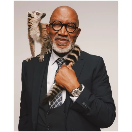 Elderly man in suit with lemur on shoulder, posing in studio. Business portrait of male with eyeglasses and exotic animal.