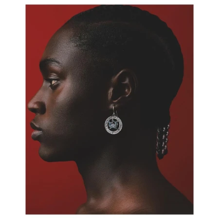 Profile portrait of a Black woman wearing a circular silver earring against a solid dark red background by photographer Aart Verrips.