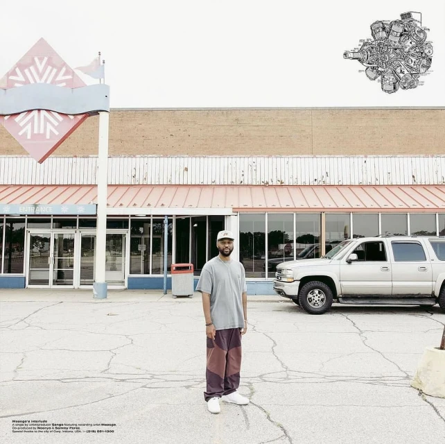 Adult male stands in front of closed retail building in an empty parking lot. A silver SUV is parked in the background.