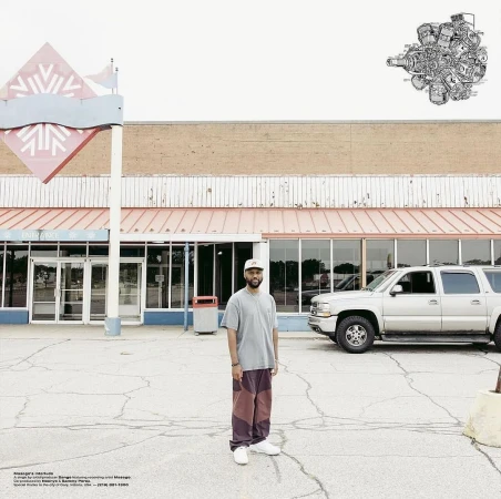 Adult male stands in front of closed retail building in an empty parking lot. A silver SUV is parked in the background.