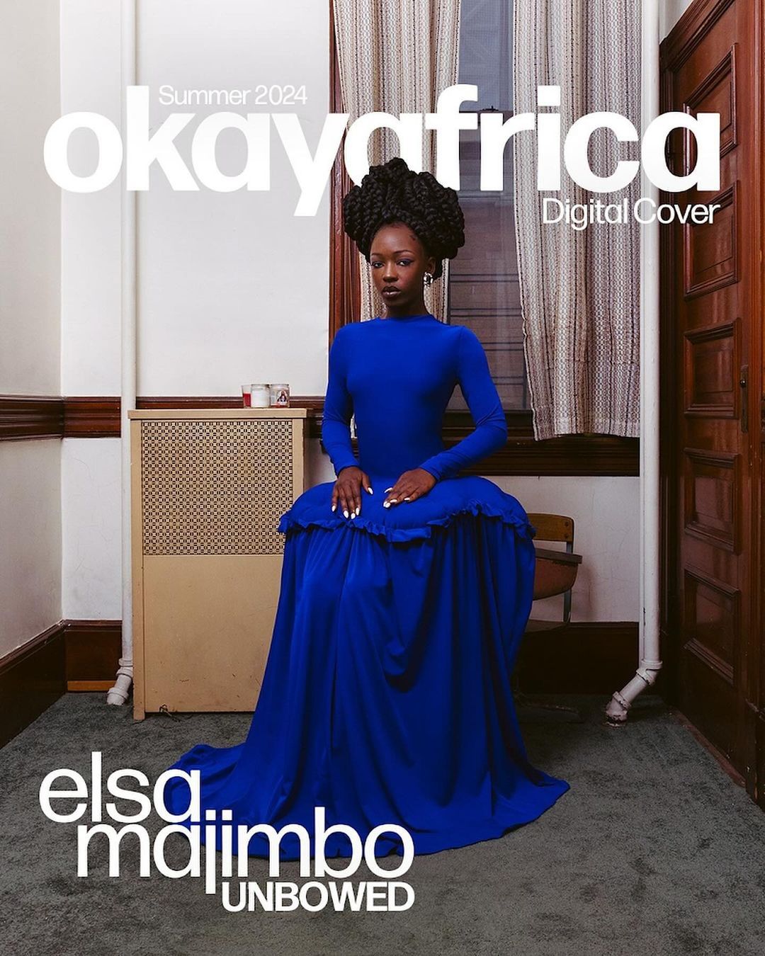 Elsa Majimbo on OkayAfrica's Summer 2024 Digital Cover, seated in a blue dress against a simple interior wall with a radiator.