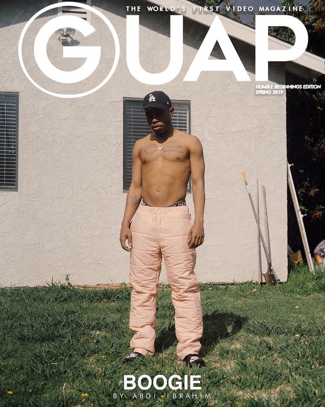 Magazine cover featuring a bare-chested man in blush quilted pants stands in a yard. The magazine's name is at the top with edition details.