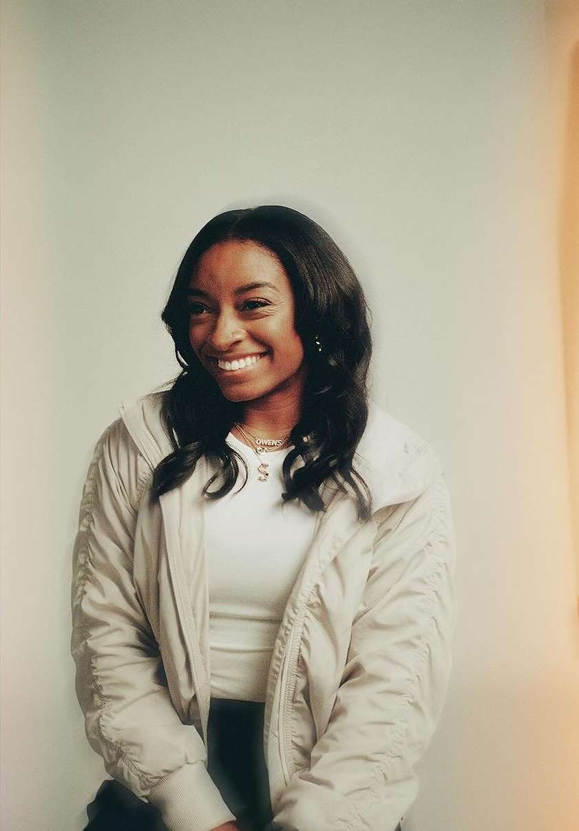 Portrait of smiling African-American woman in bomber jacket. Head and shoulders shot against a white backdrop with soft studio lighting.
