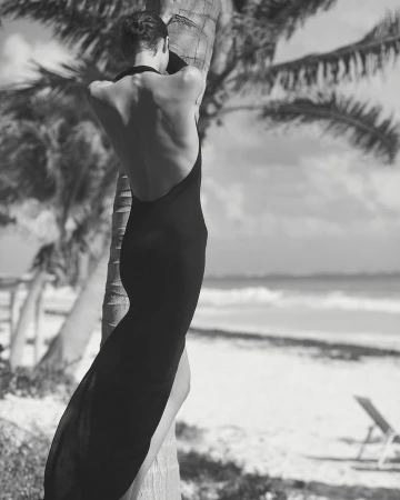 Model in a black backless dress leaning against a palm tree on a tropical beach in Los Angeles by Adam Franzino