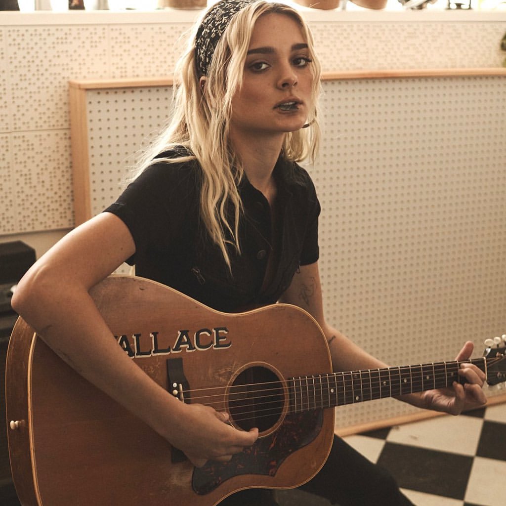 Young adult female musician plays a vintage acoustic guitar while wearing a black shirt and patterned headband in a music studio.
