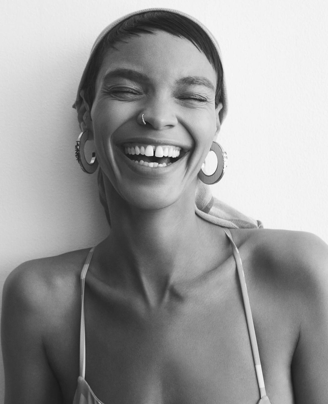 Portrait of a laughing woman wearing hoop earrings and a headscarf against a plain background