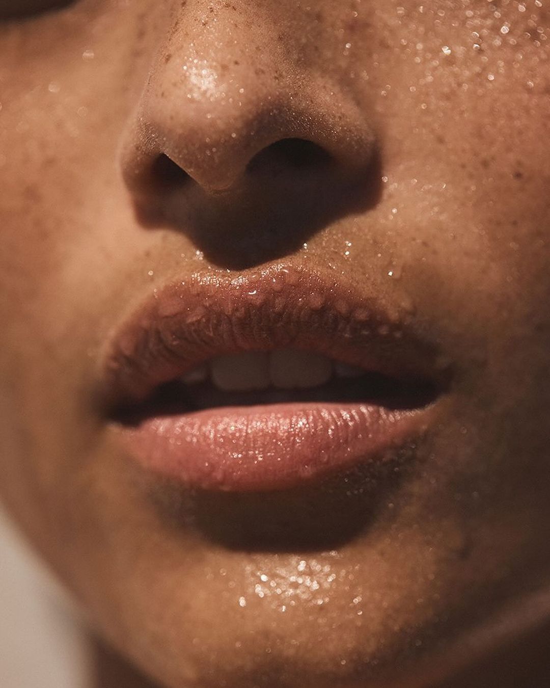 Close-up on an adult female's face featuring freckles, skin glistening with moisture, nose, lips, and teeth in soft, diffused lighting.