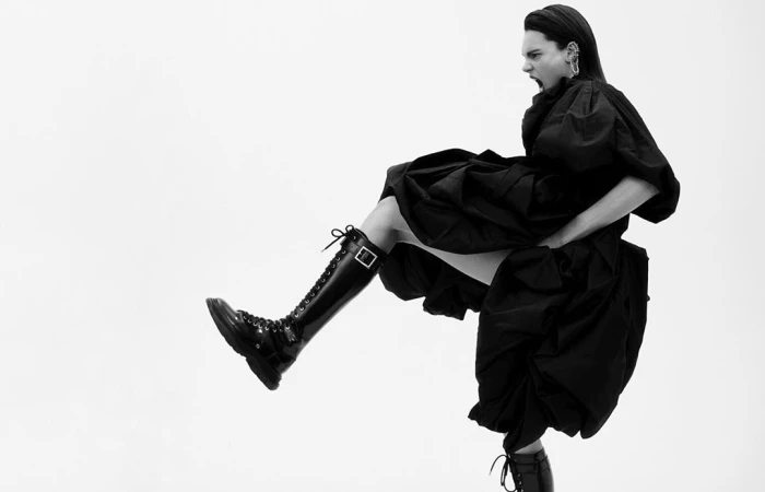 Model in black dress and patent combat boots kicking mid air by Adam Franzino