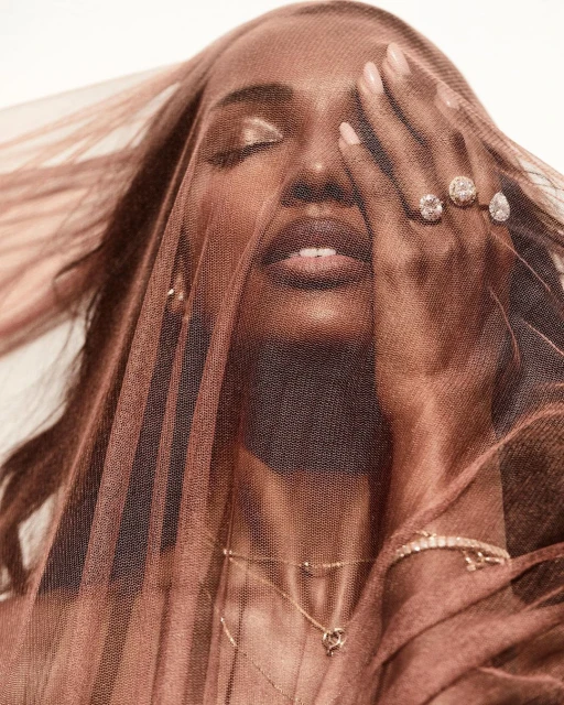 Close-up studio portrait of an adult woman partially veiled, wearing diamond jewelry, neutral makeup, against a white background.