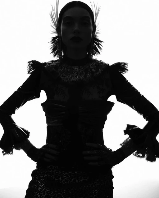 Monochromatic portrait of a stylish woman in an ornamental top and headdress, set against a bright, plain background.