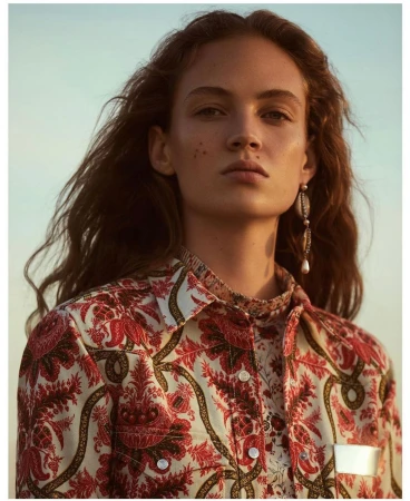 Close-up portrait of a woman wearing a red and white patterned shirt and drop earrings against a clear sky
