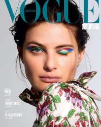 Close-up portrait of a woman with vibrant blue and green eyeshadow wearing a floral print top