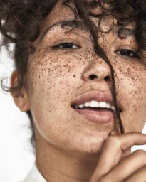 Close-up portrait of a woman with heavy freckles and dark curly hair by photographer Adam Franzino