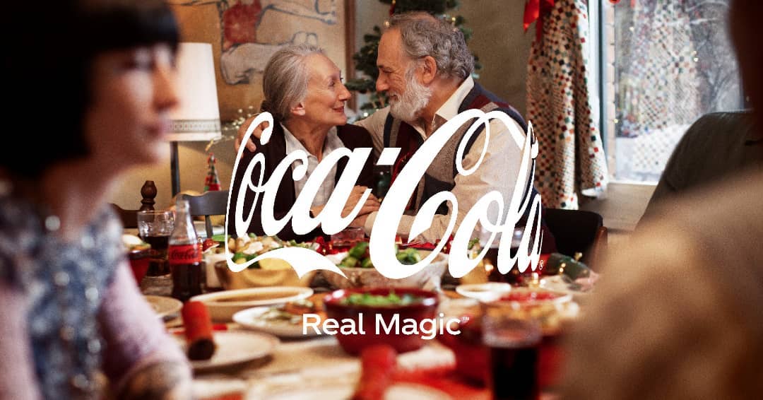 Coca-Cola advertisement showing an elderly couple smiling across a dinner table with a large Coca-Cola logo superimposed.