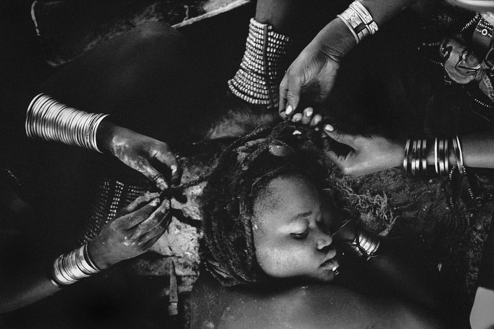 Close-up black and white portrait of a woman's face and hands adorned with traditional metal bracelets styling her dreadlocks.