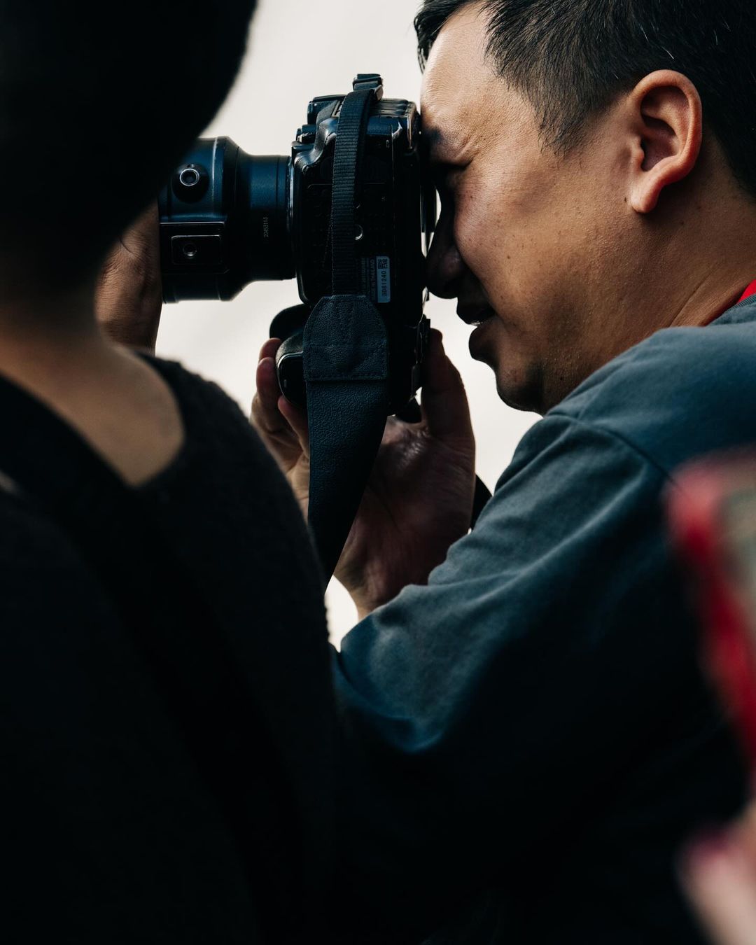 Adult male photographer with professional camera taking a picture. Shoulder of a second person also appears in the photo.